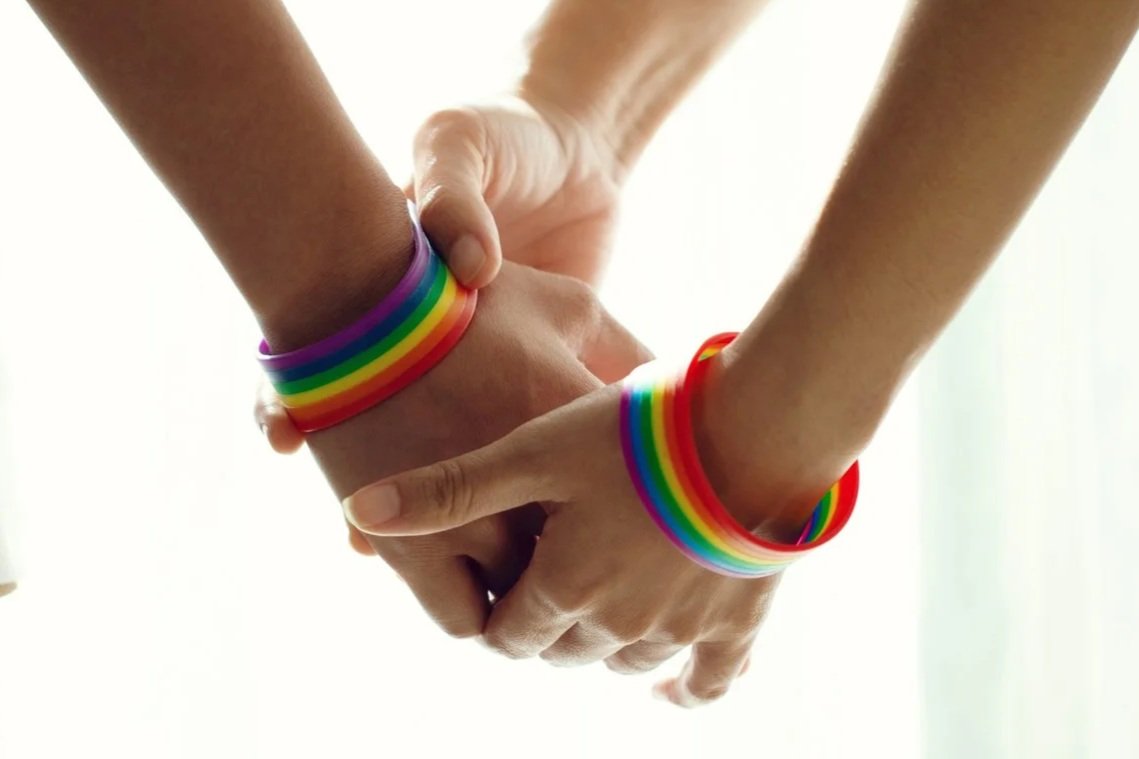 Two people holding hands, each wearing rainbow-colored bracelets.