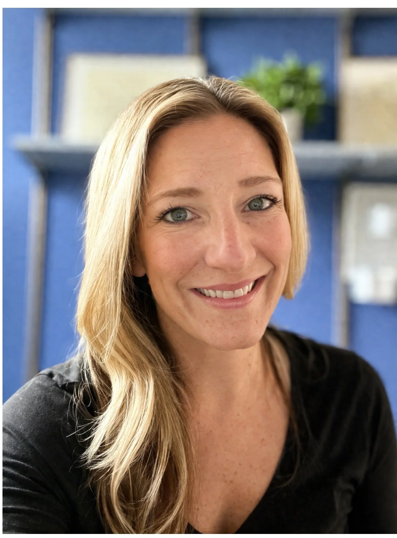 Smiling therapist with shoulder-length hair seated in a warm, softly lit setting, creating a welcoming and approachable presence.