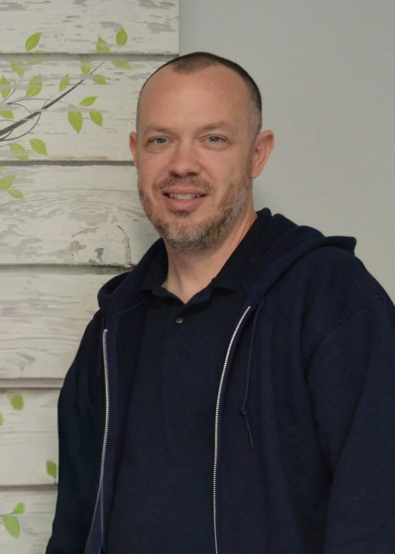 Friendly recovery coach smiling in a welcoming setting, conveying approachability, lived experience, and supportive guidance for individuals in addiction and mental health recovery.