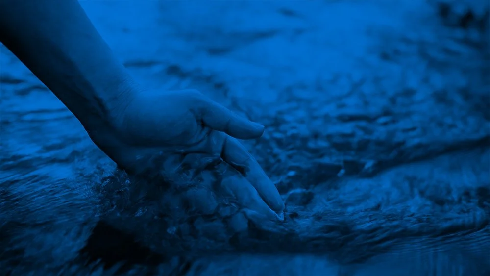 Close-up of a person's hand submerged in flowing water, touching the surface.