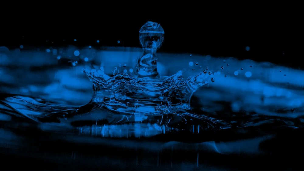 Close-up of a water droplet splash in the dark, illuminated with blue light.