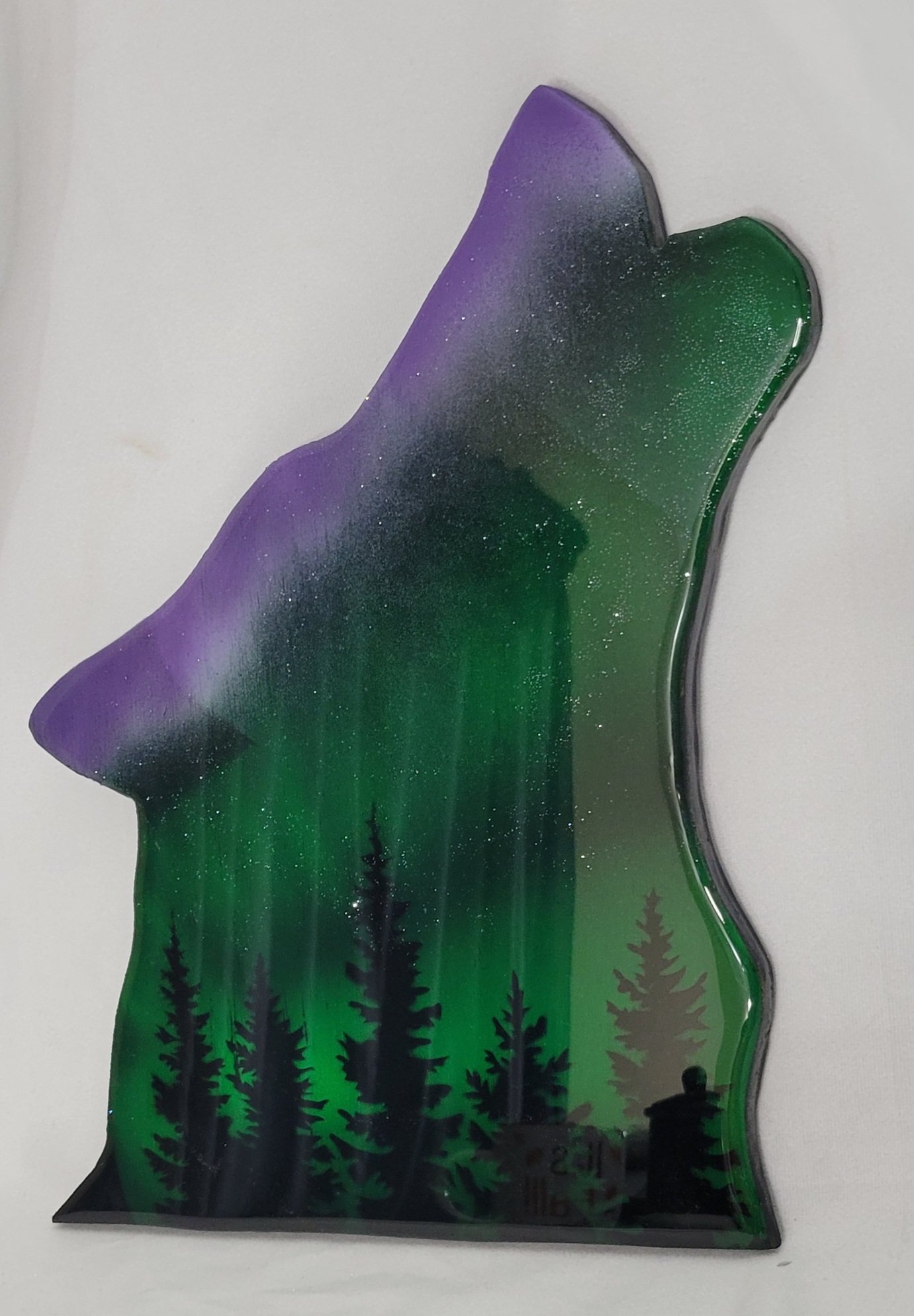 A epoxy resin art piece shaped like a bear's head with a skyline of pine trees at the bottom, featuring purple and green colors with a starry effect.