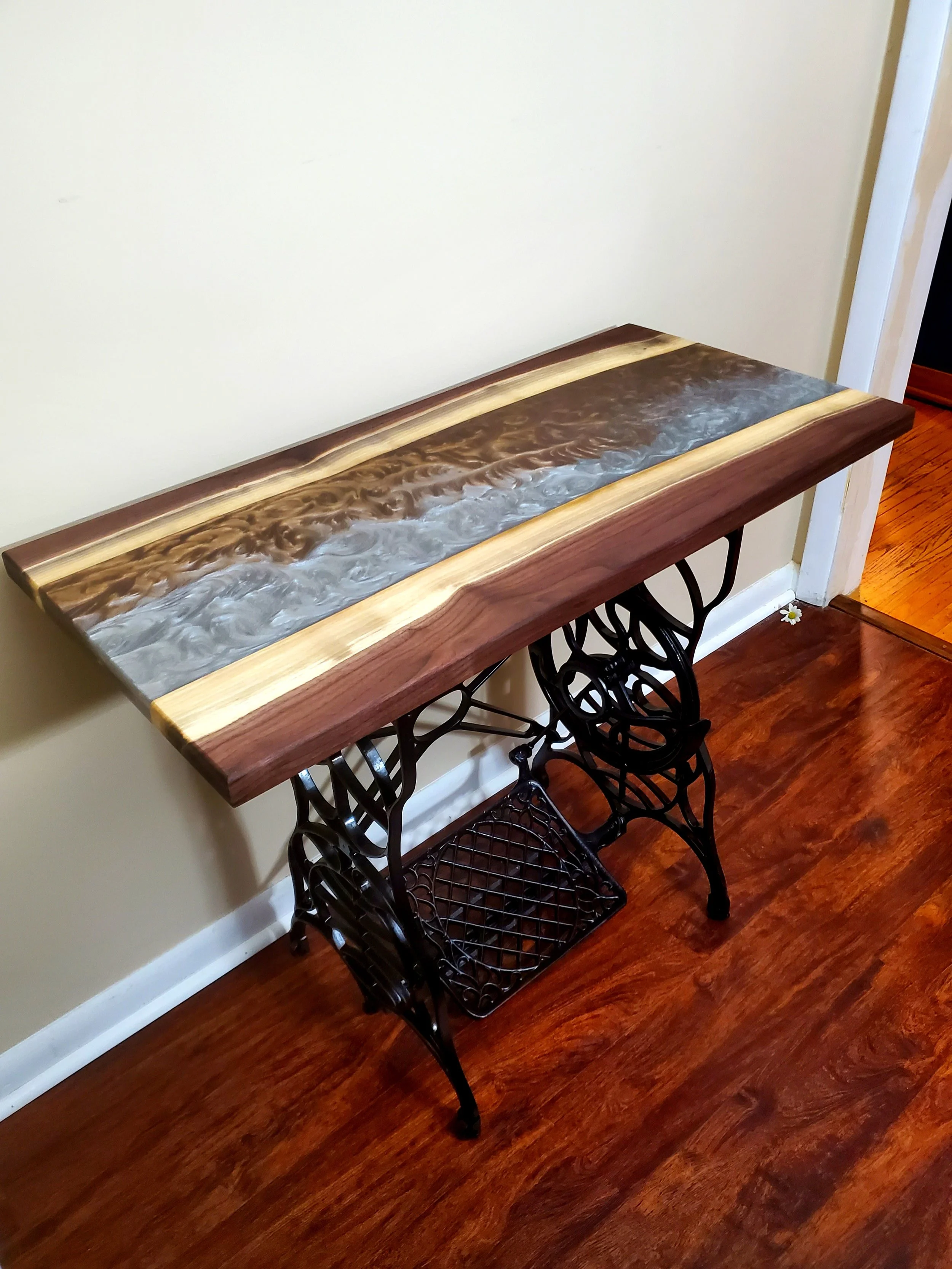 A decorative table that combines a vintage sewing machine base with a wooden table top featuring a river of resin art.