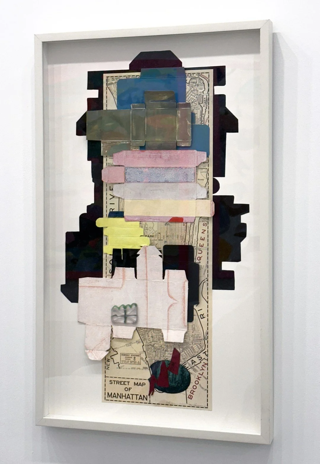 Collage artwork featuring layered cutouts of various paper materials, including maps, receipts, and colorful shapes, arranged vertically on a background of a Manhattan street map.