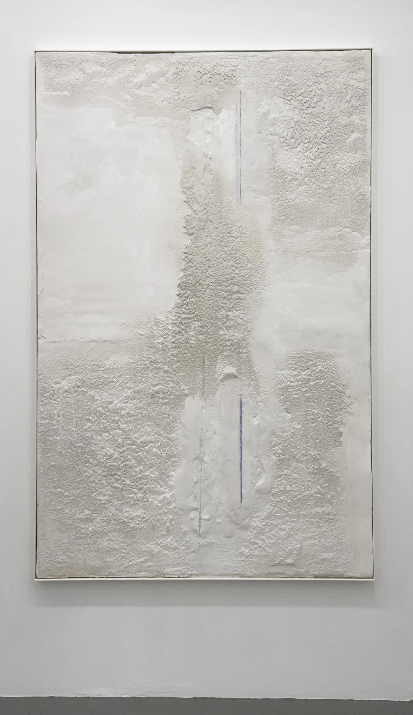 Abstract textured white painting with subtle blue vertical line in the center, framed on a white wall.