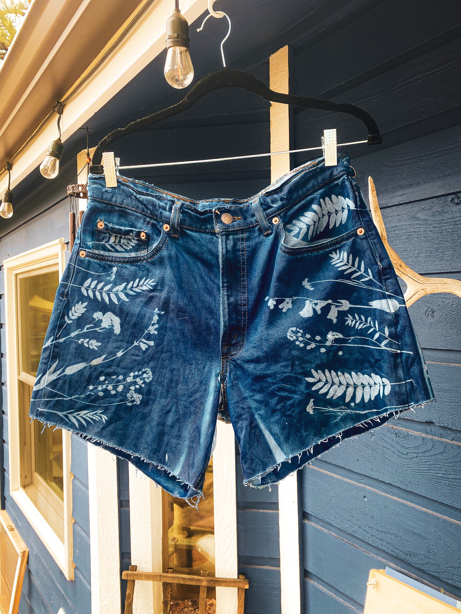Blue denim shorts with floral patterns hanging on a clothesline.