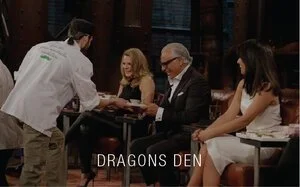 A restaurant scene at Dragons Den with four people seated at a table and a chef serving them.
