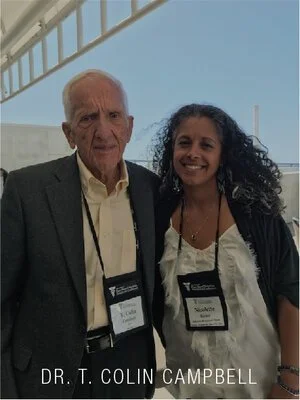 An elderly man and a young woman standing together at an indoor event, both wearing name tags and smiling for the photo.