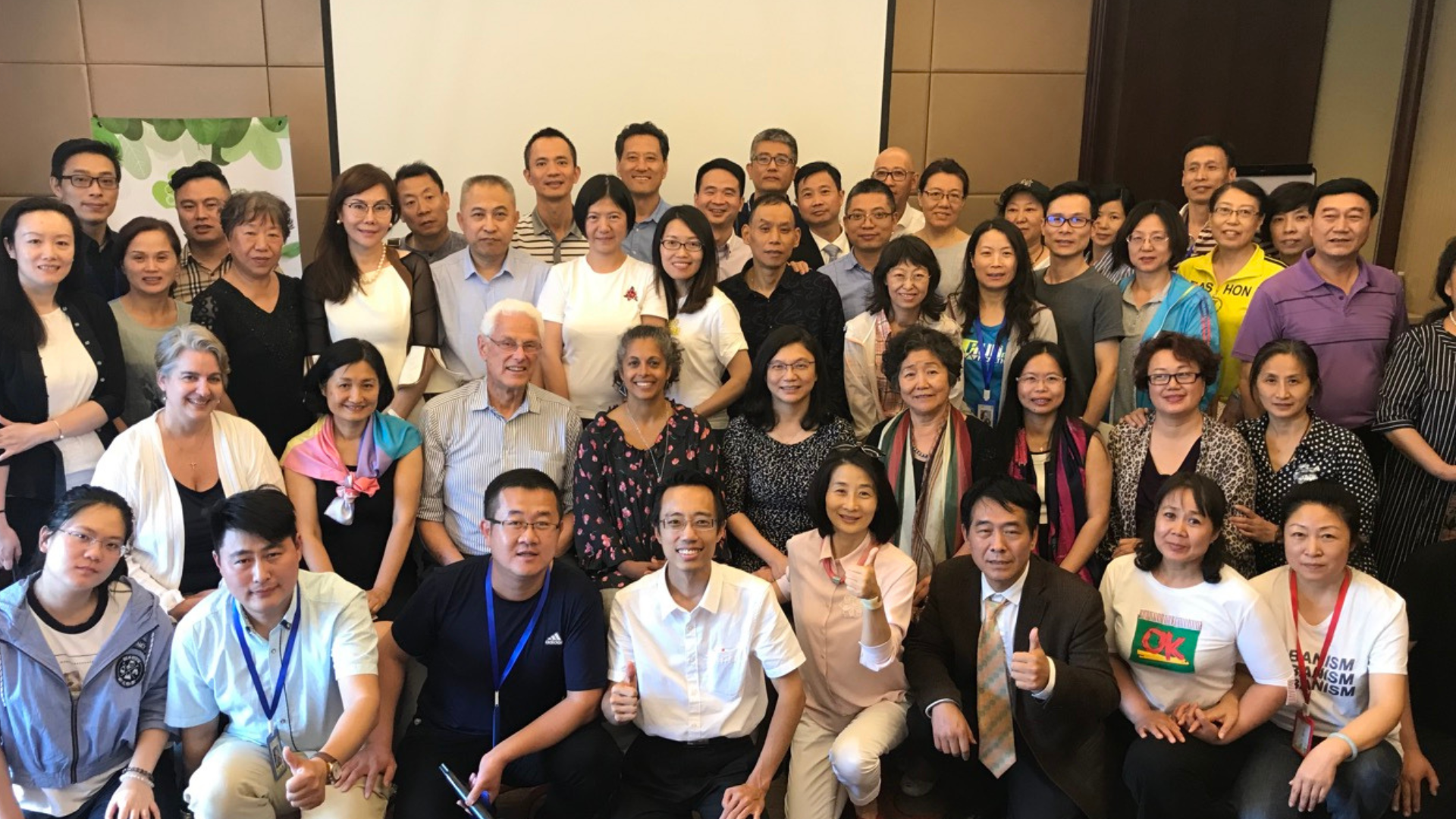 A large group of diverse people gathered indoors for a group photo, smiling and posing.
