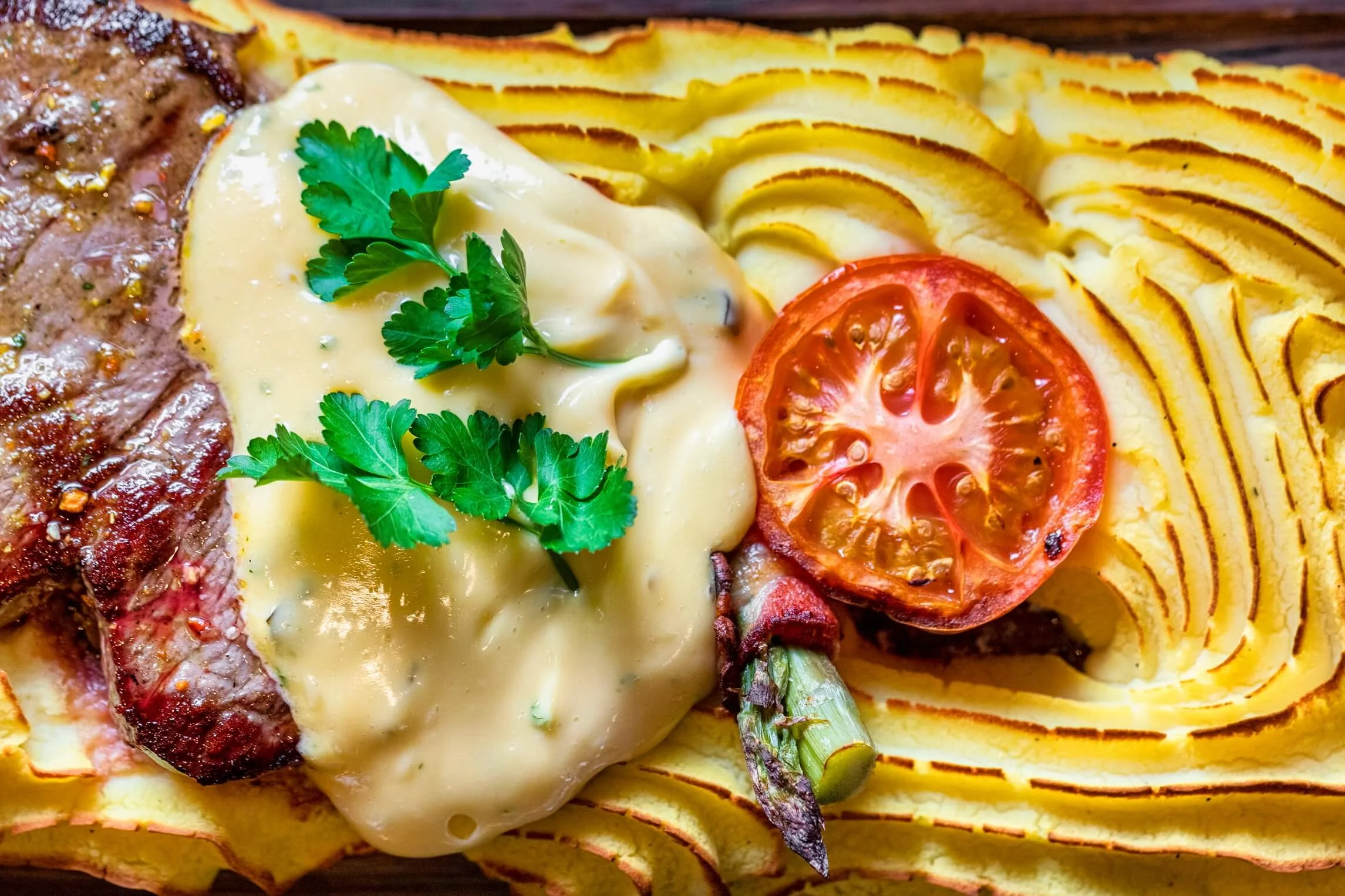 Baked potato with broccoli and cheese, topped with chopped tomatoes and cilantro, served with a steak.