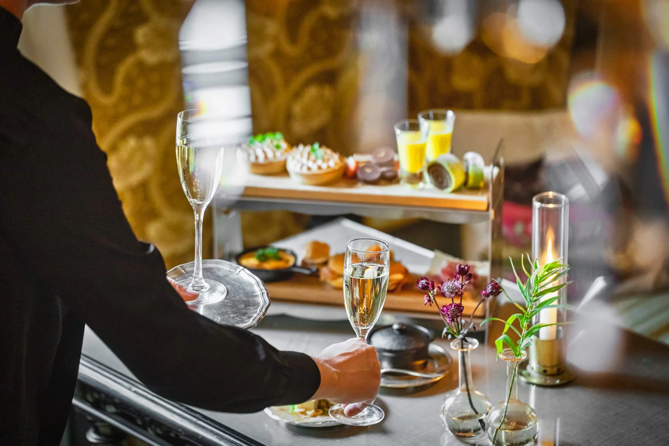 A person in black attire holding a champagne glass at a celebration table with food and drinks.