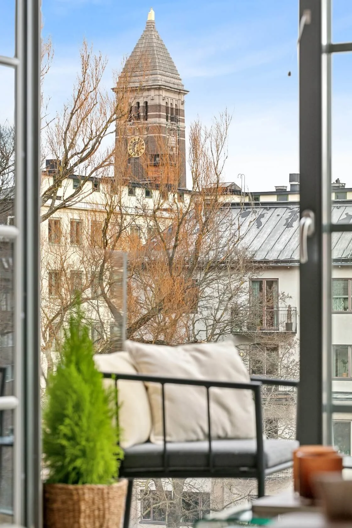 View from a balcony showing a historic clock tower and residential buildings with leafless trees.