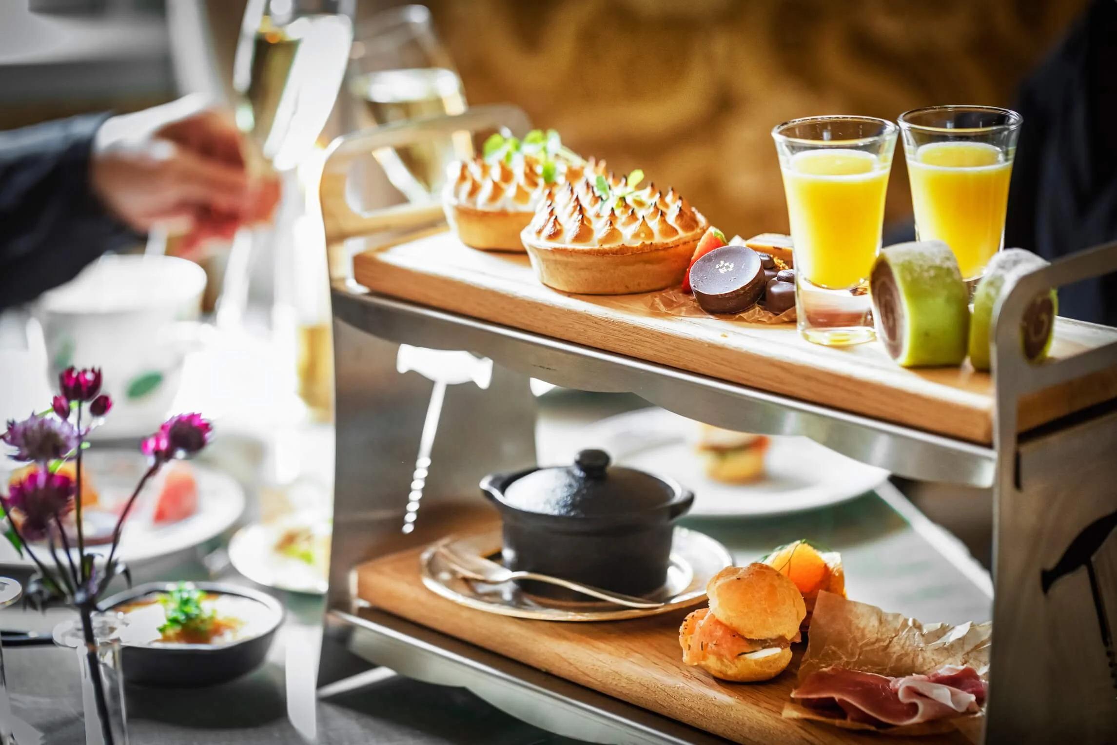 A multi-tiered tray with breakfast items including waffles, coffee, juice, bread rolls, fruit, and spreads, set on a table in a cozy setting.