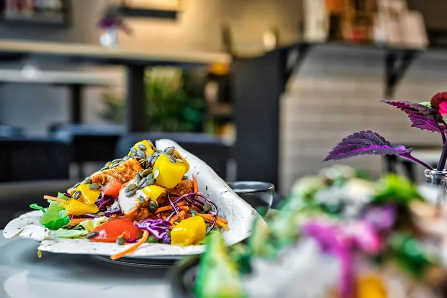 A loaded taco on a plate with various colorful vegetables, seeds, and toppings, placed on a table outside.