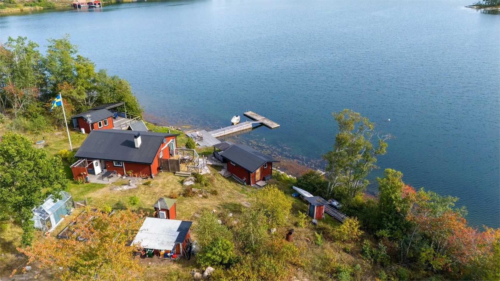 Aerial view of a lakeside property with red houses, a dock, boats, and surrounding trees.