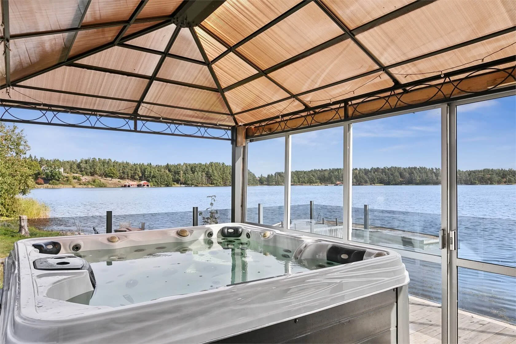 Hot tub on a screened porch overlooking a lake with trees and blue sky in the background.