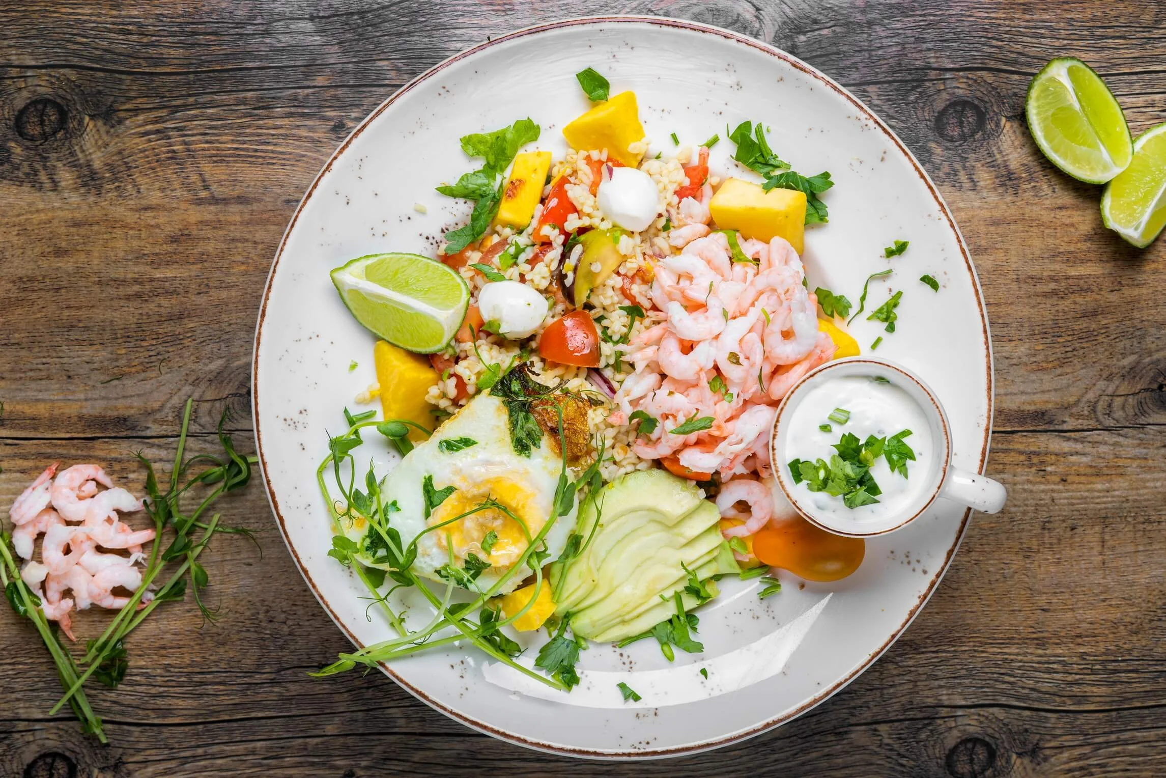 A plate of Shrimp and Mango Salad with lime wedges and a side of creamy dressing with chopped herbs