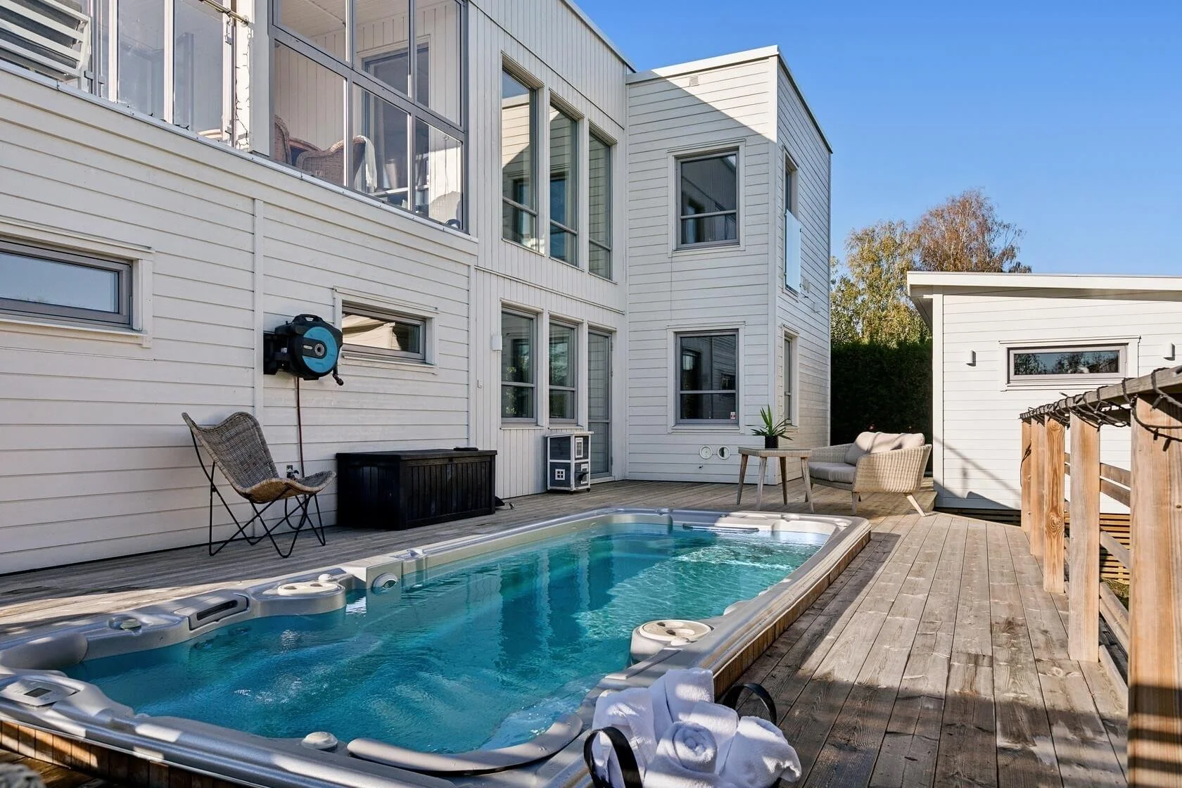 Outdoor backyard with hot tub, seating, and modern white house with multiple windows and a wooden deck.