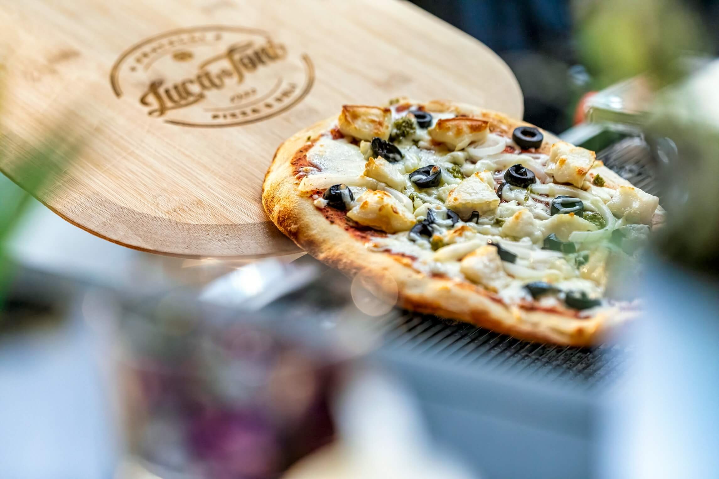 A slice of pizza with cheese, chicken, black olives, and green peppers on a wooden pizza peel.