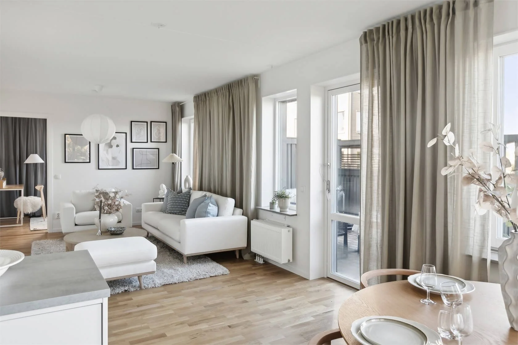 Bright living room with white sofa, beige curtains, hardwood floor, and decorative wall art.