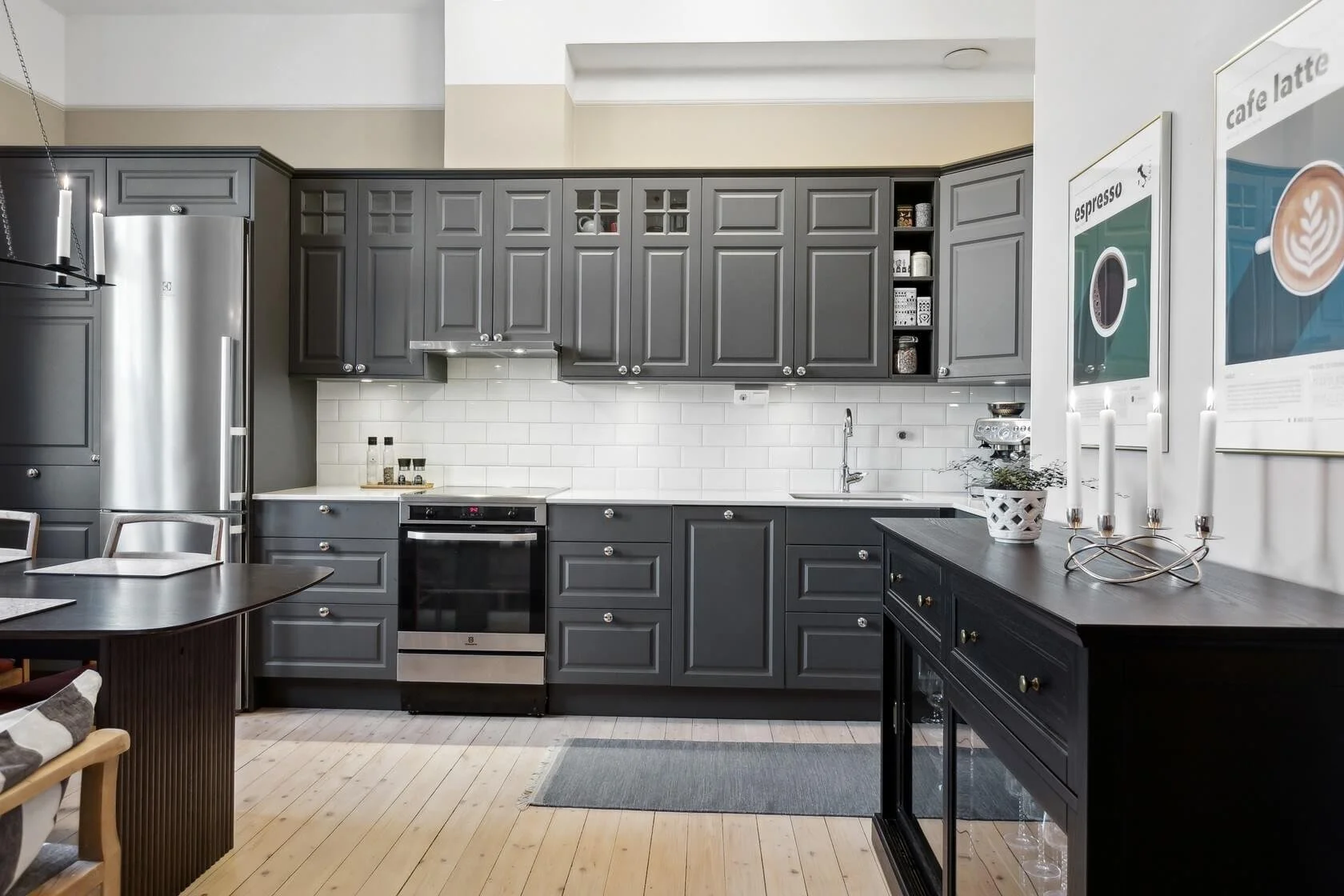Modern kitchen with gray cabinets, stainless steel refrigerator, white subway tile backsplash, and wooden flooring.