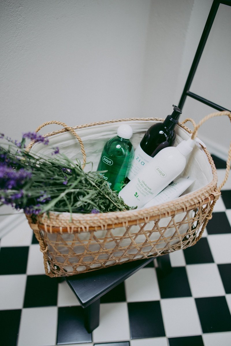 Basket with Ziaja skincare bottles and lavender on checkered floor.