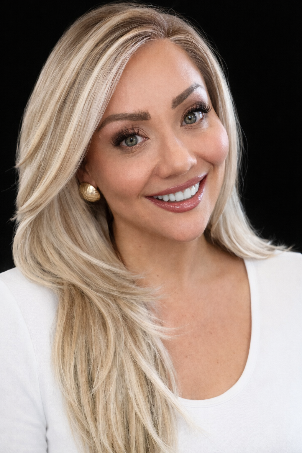 professional blonde woman smiling wearing a white top and gold earrings