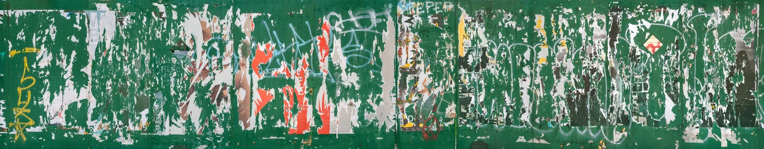 Fine art urban photography capturing decaying advertising posters on a plywood construction site fence. The composition isolates layers of shredded commercial paper, weathered textures, and accidental street art by Barton Lewis.