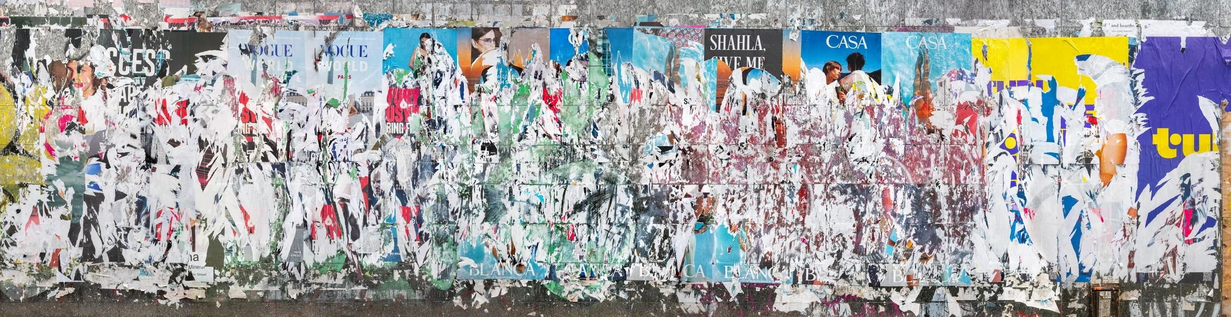 Fine art urban photography capturing decaying advertising posters on a plywood construction site fence. The composition isolates layers of shredded commercial paper, weathered textures, and accidental street art by Barton Lewis.