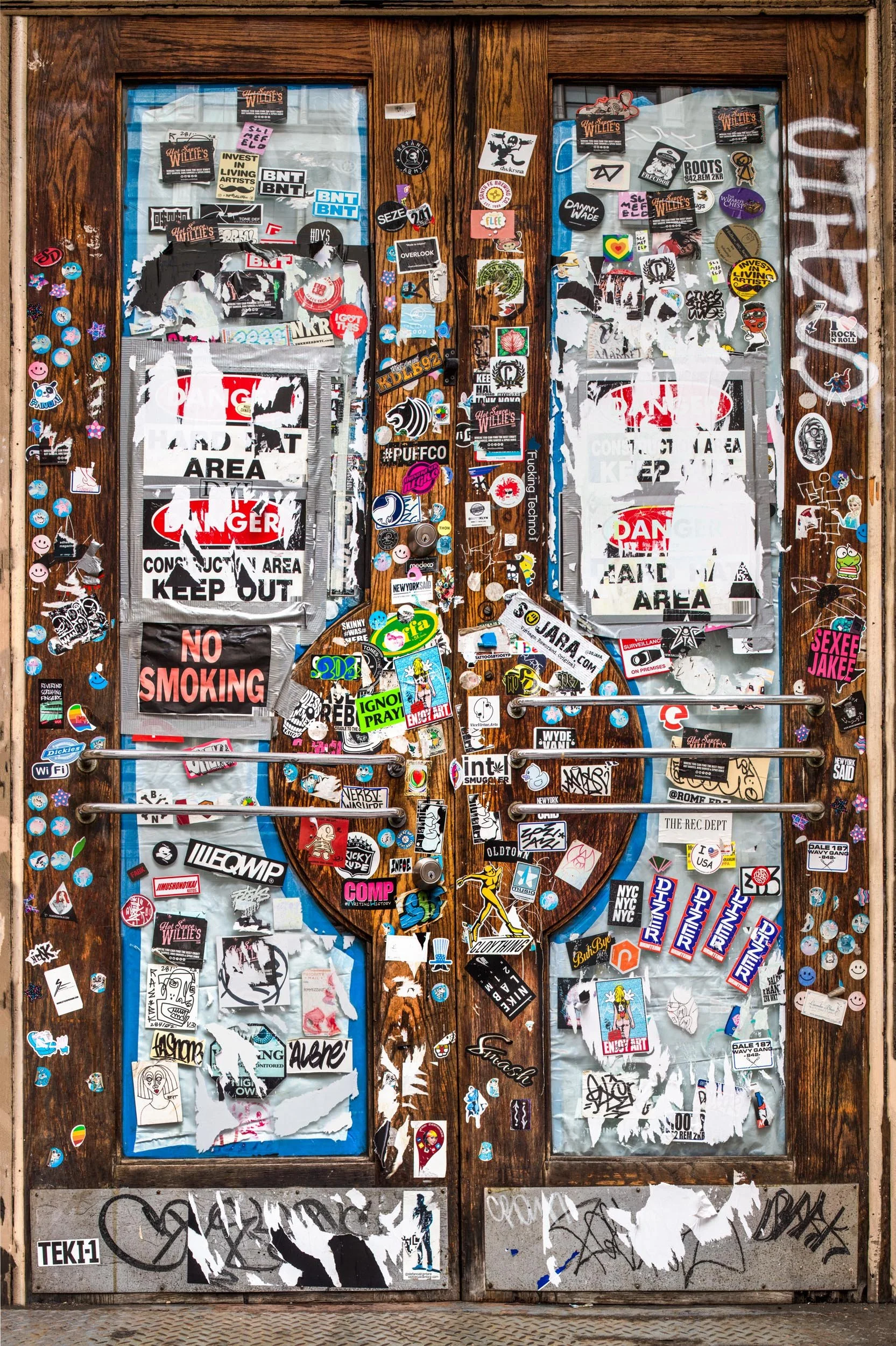 Fine art urban photography print of a door in New York City entirely covered in layers of sticker slaps. This example of collaborative and impromptu street art is captured by contemporary photographer Barton Lewis.