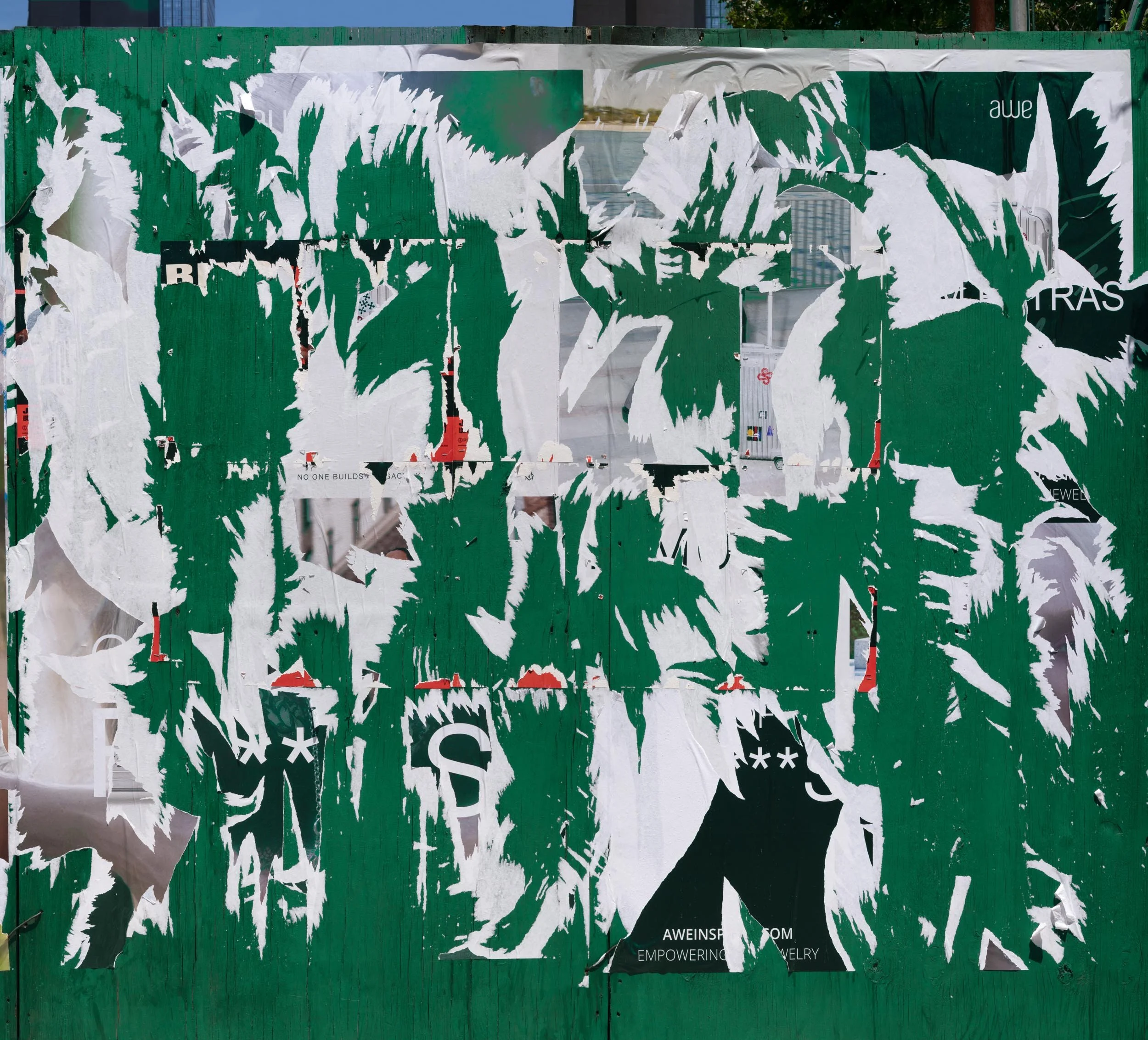 Fine art urban photography capturing decaying advertising posters on a plywood construction site fence. The composition isolates layers of shredded commercial paper, weathered textures, and accidental street art by Barton Lewis.