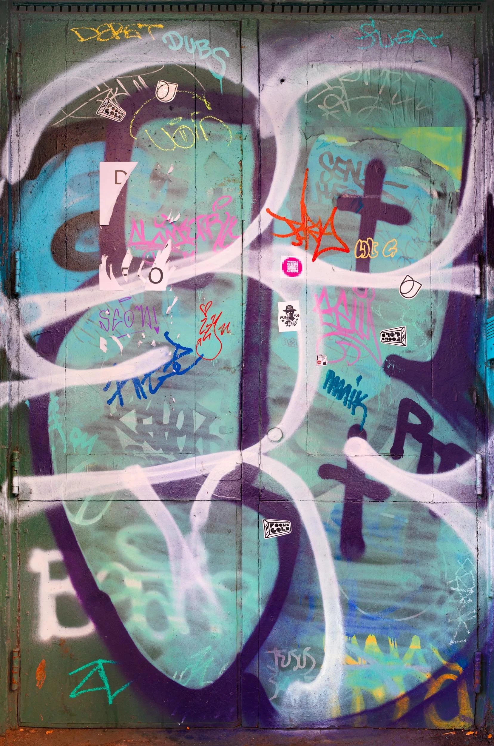 Fine art urban photography print of a door in New York City covered with graffiti, p;aint and some sticker slaps. This example of collaborative and impromptu street art is captured by contemporary photographer Barton Lewis.