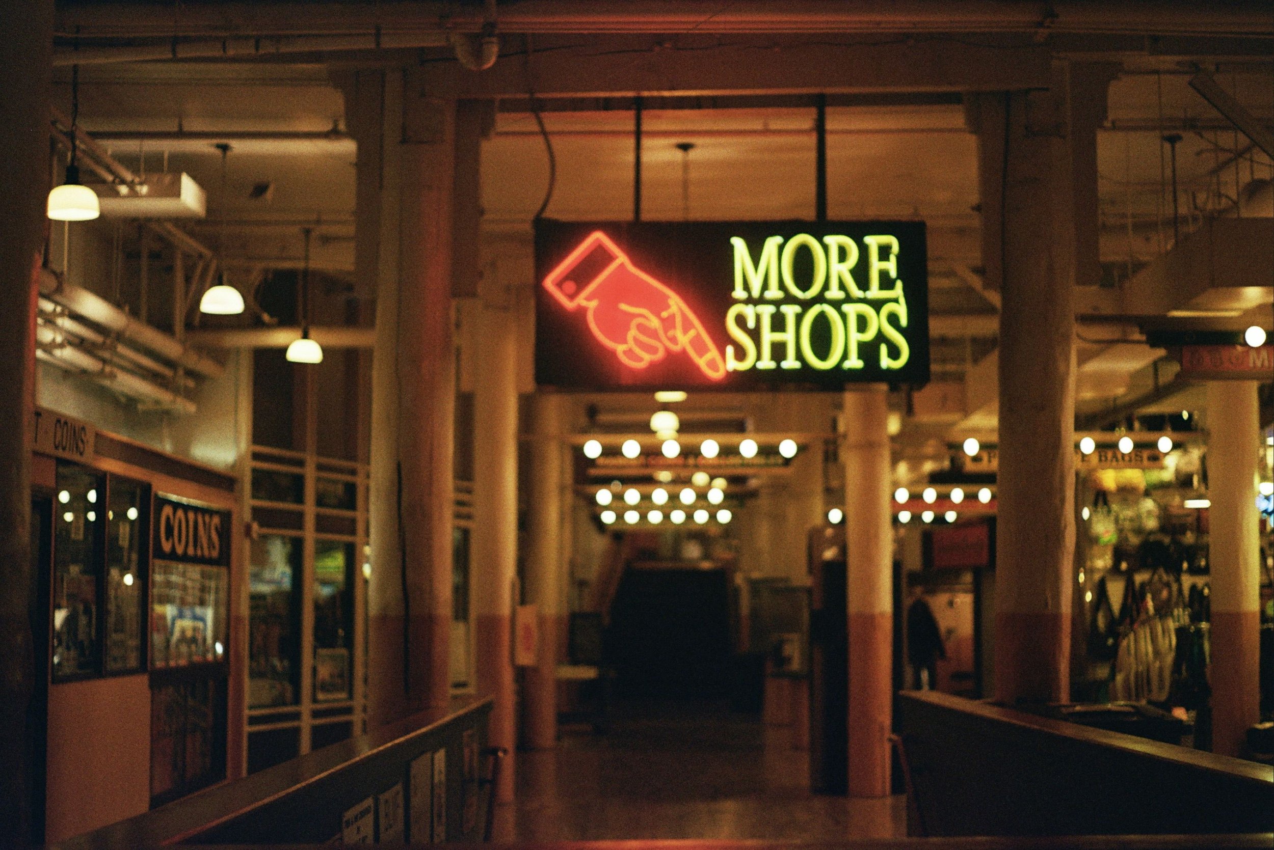 Vintage indoor shopping area with neon sign highlighting more shops and coins shop.
