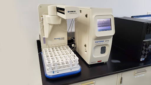 Laboratory instrument with a sample rack, computer screen, and other equipment on a black countertop.