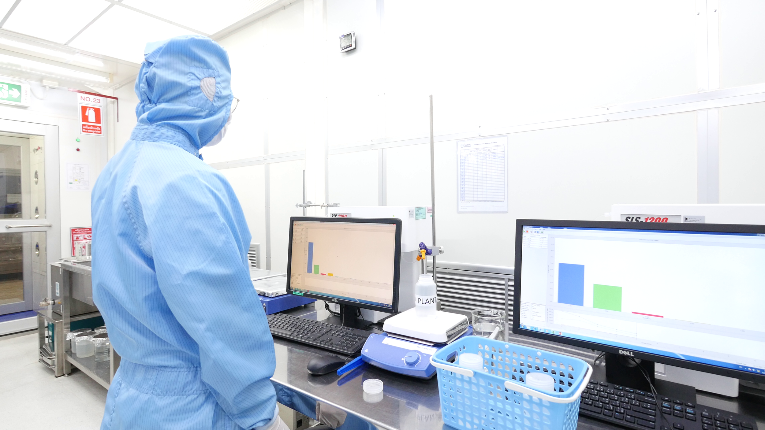 A scientist in a blue protective suit working with laboratory equipment and computers in a clean laboratory environment.