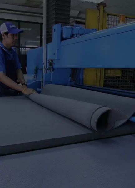 A worker operates a large industrial machine cutting or handling a large sheet of fabric or material in an industrial setting.