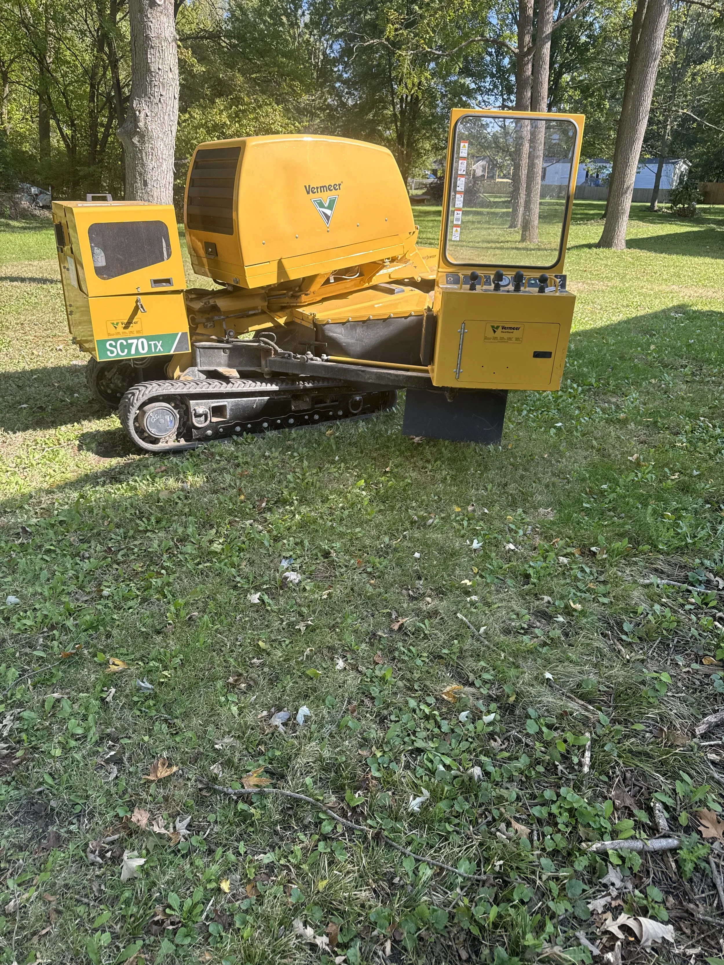Yellow Vermeer SC70TX remote-controlled construction or landscaping robot on grass with trees and houses in the background.