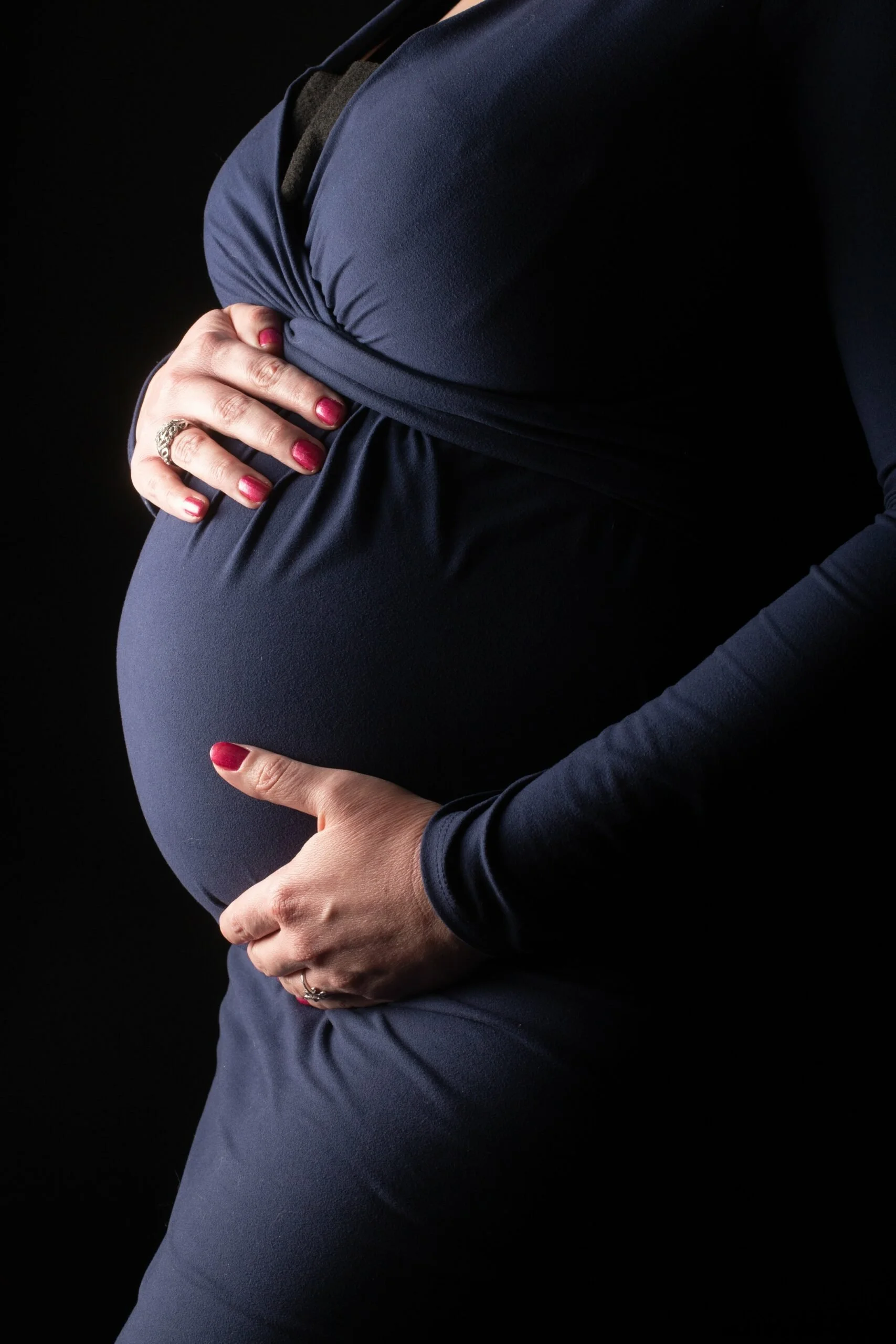 Close-up of pregnant woman's belly with hands cradling the bump during an intimate maternity portrait session at Say Yes to Jess Cincinnati