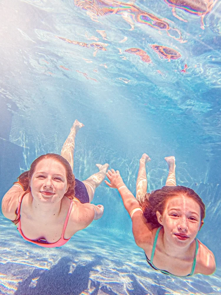 Two girls smiling and making silly faces underwater during an underwater photography session at Say Yes to Jess in Cincinnati and Northern Kentucky