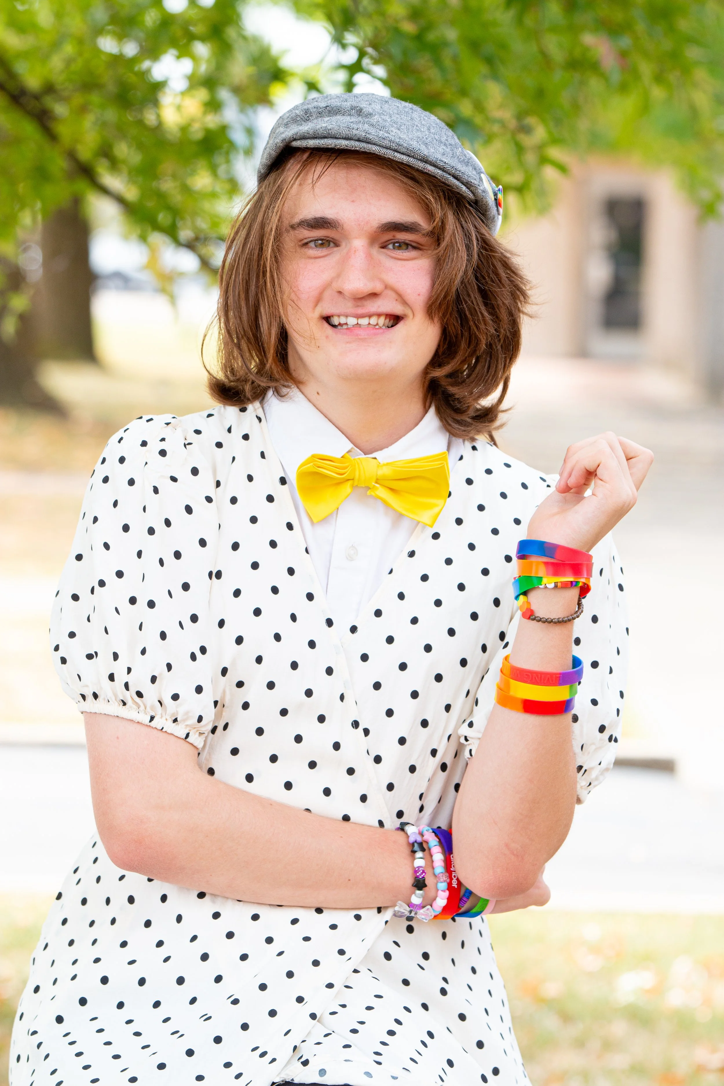 Student in polka dot shirt and yellow  bowtie with rainbow bracelet posing for  outdoor school portrait 