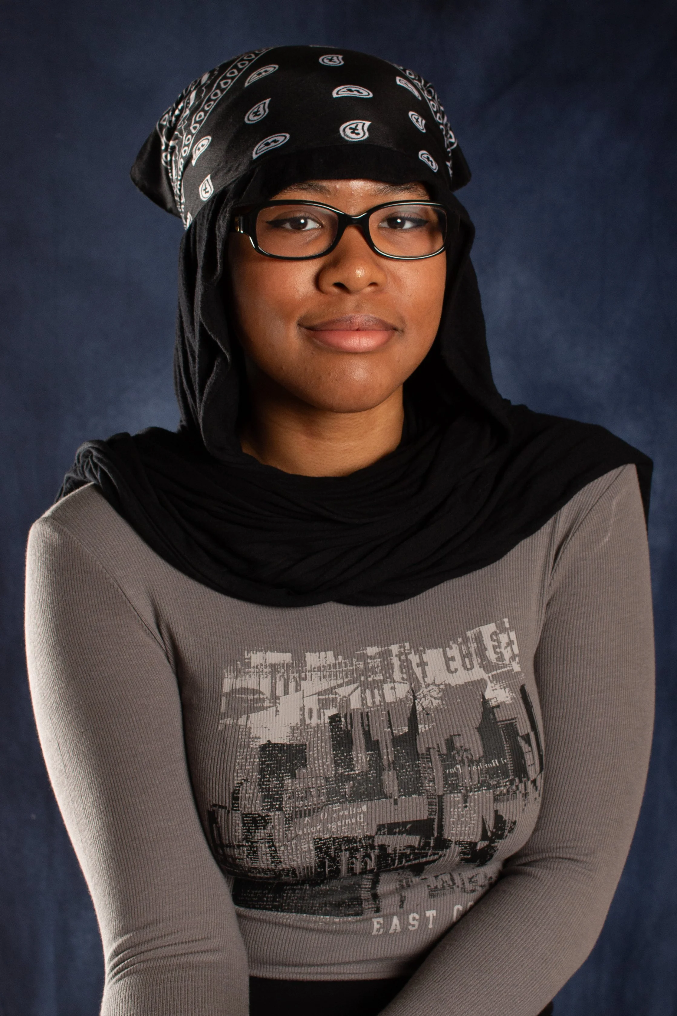 Student wearing headscarf and glasses posing for school portrait with dark studio backdrop