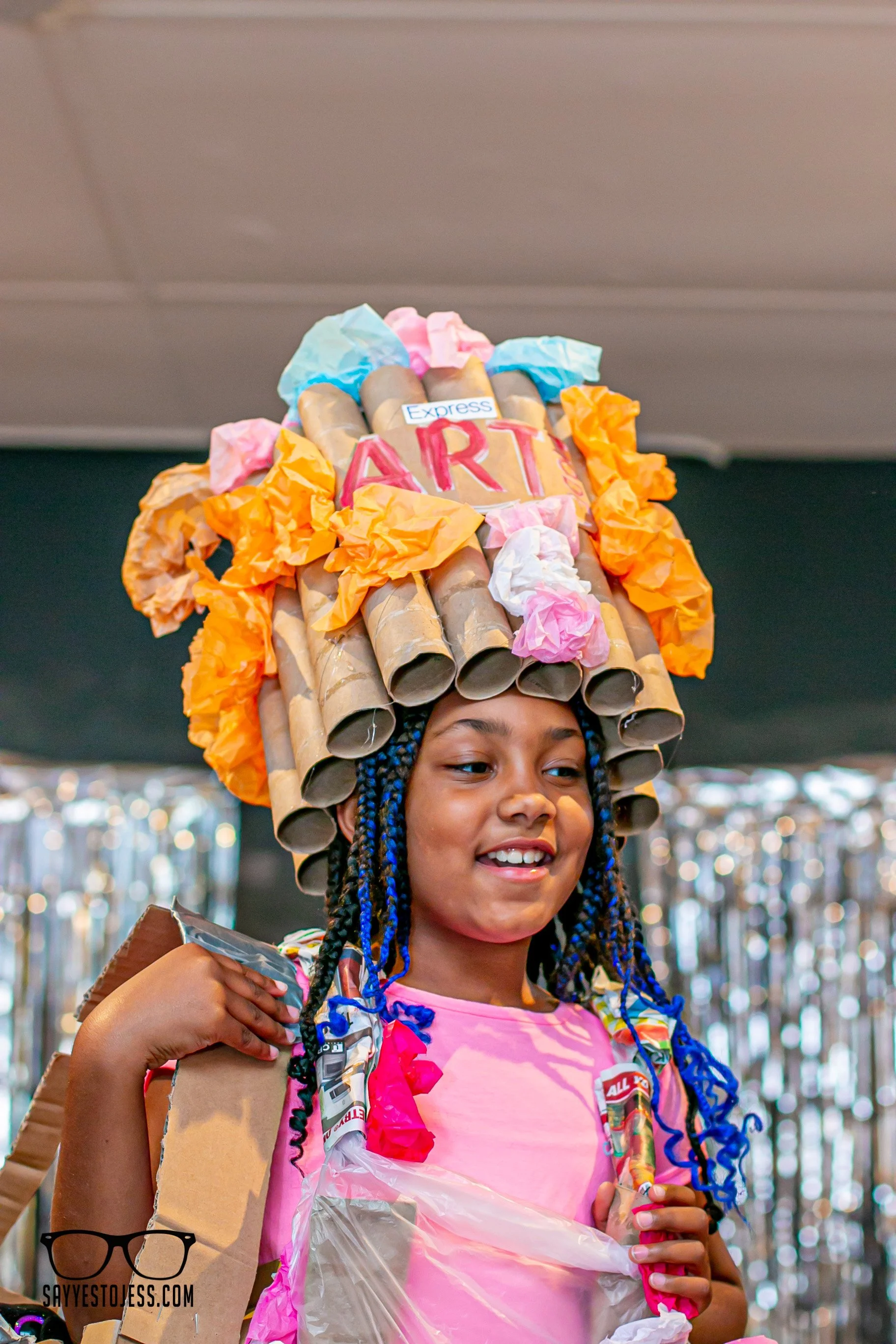 Close up of girl smiling and showing off her recycled art headpiece made from cardboard tubes and tissue paper