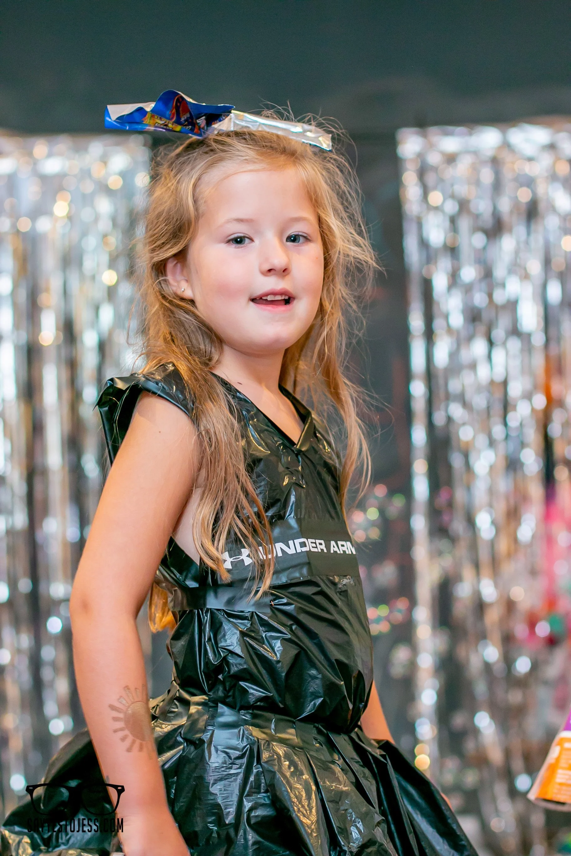 Young girl posing on the runway in a dress made from recycled black trash bags with a silver bow headpiece
