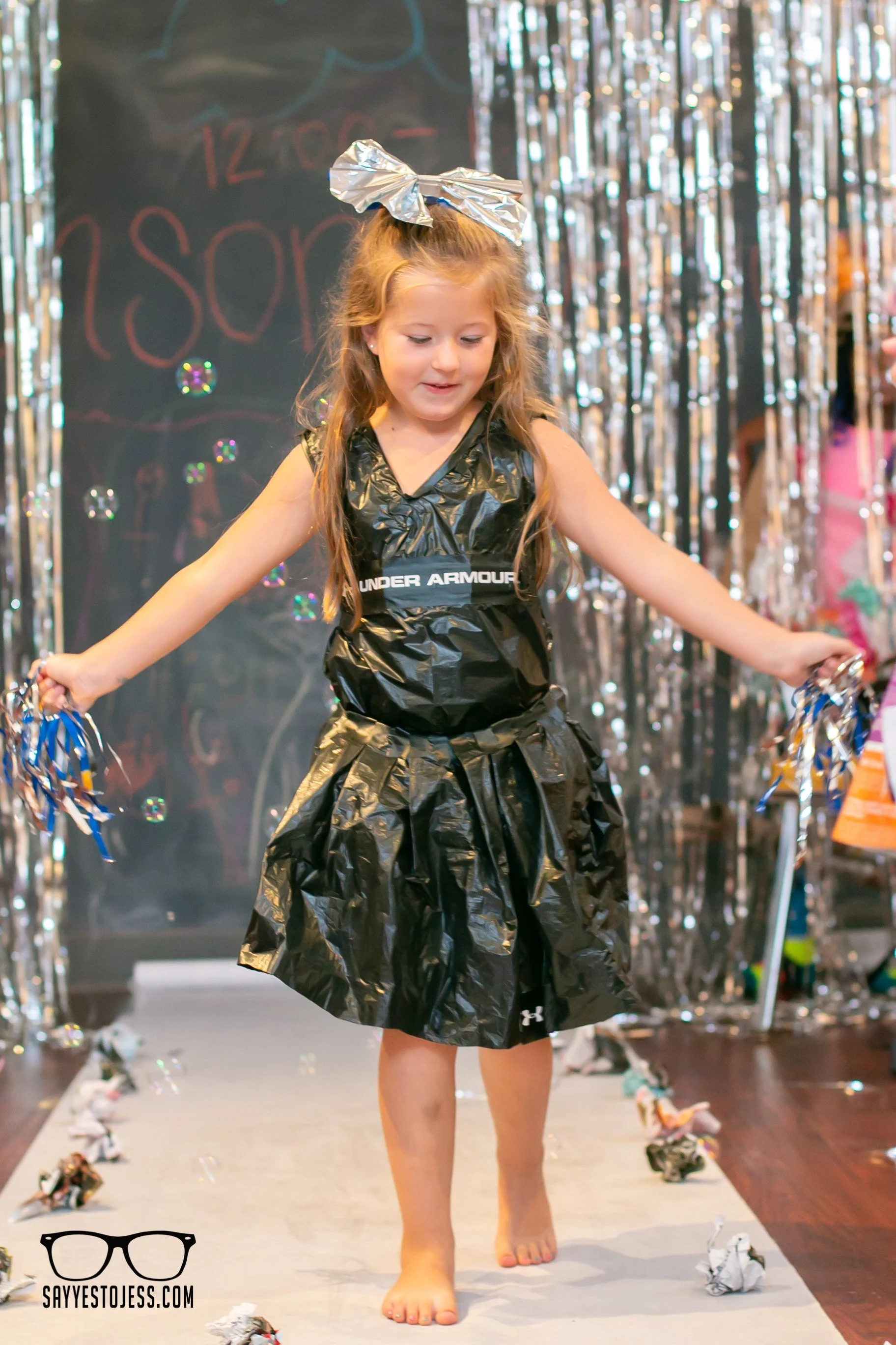 Girl in recycled trash bag dress walking the runway with tinsel streamers at the kids trashion show in Cincinnati