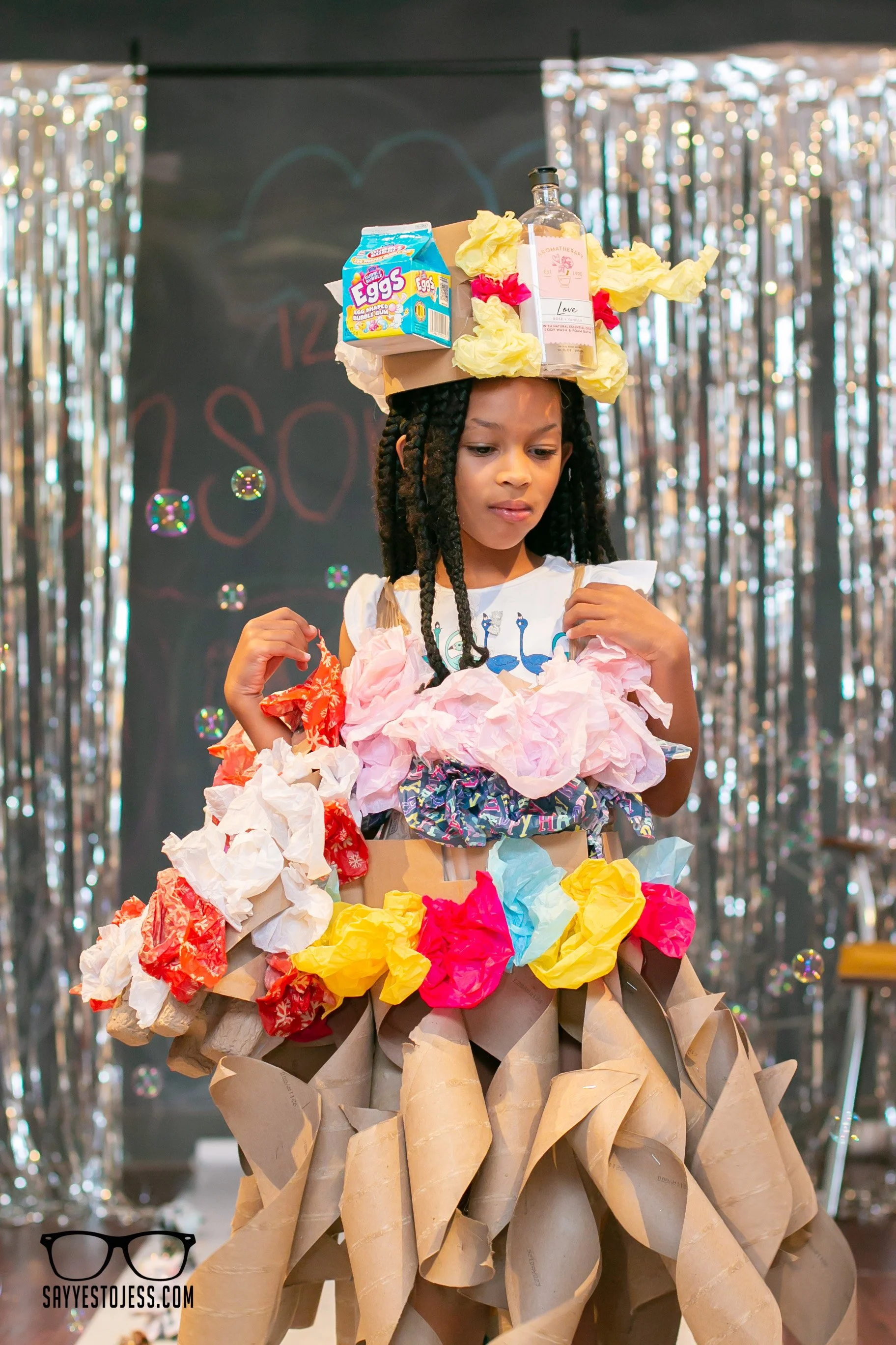 Girl in recycled materials outfit walking the runway with bubbles at Say Yes to Jess kids trashion show