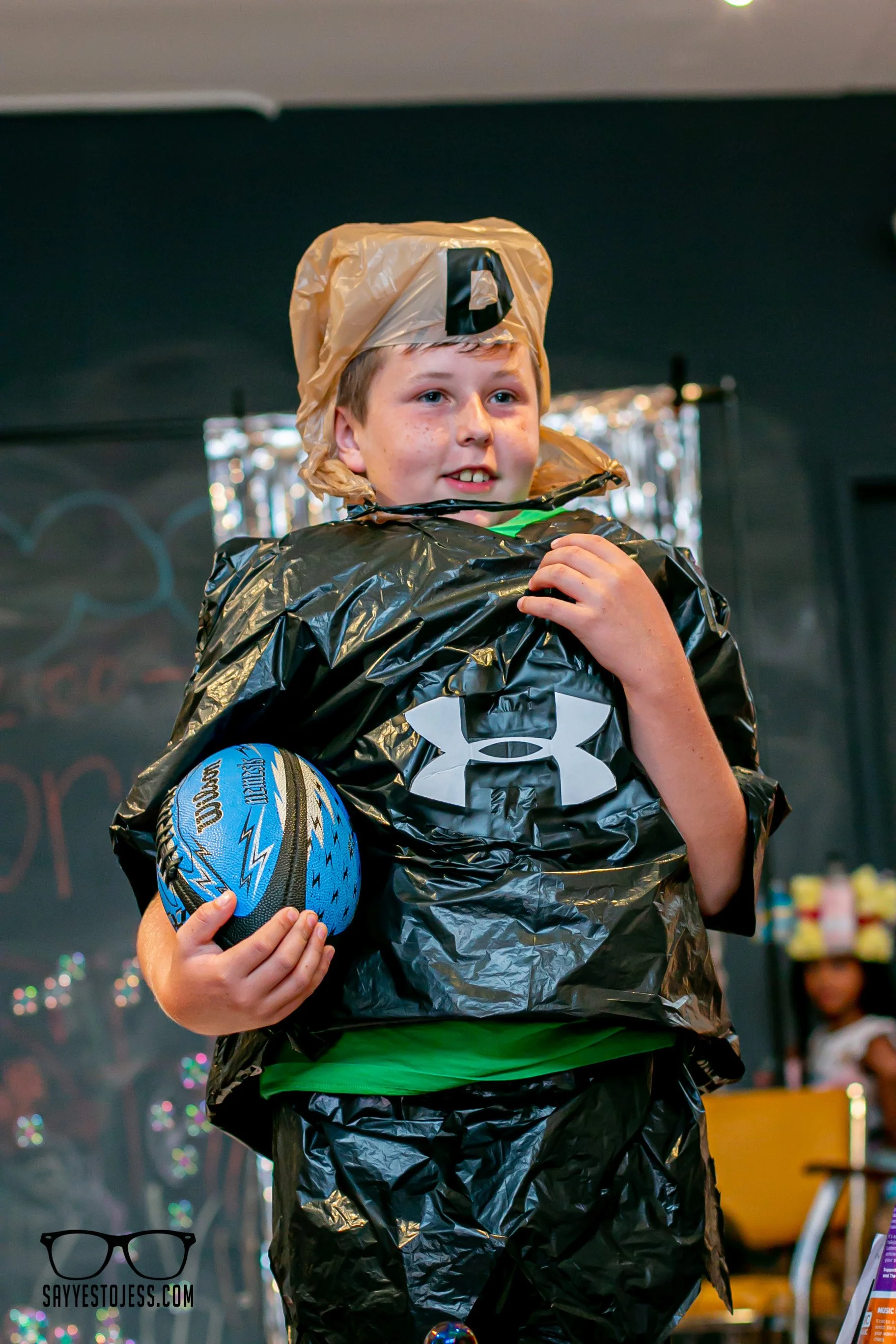 Boy in recycled trash bag outfit holding a basketball walking the trashion show runway