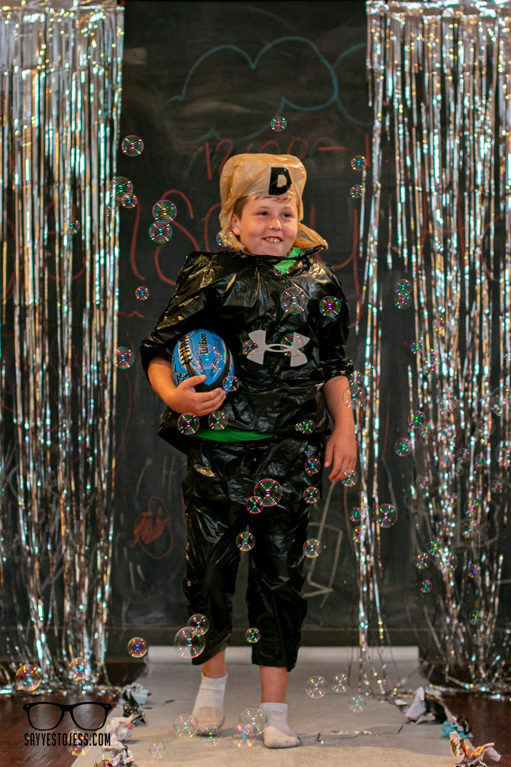 Boy in recycled trash bag outfit with basketball surrounded by bubbles on the runway at Red Balloon Cafe trashion show