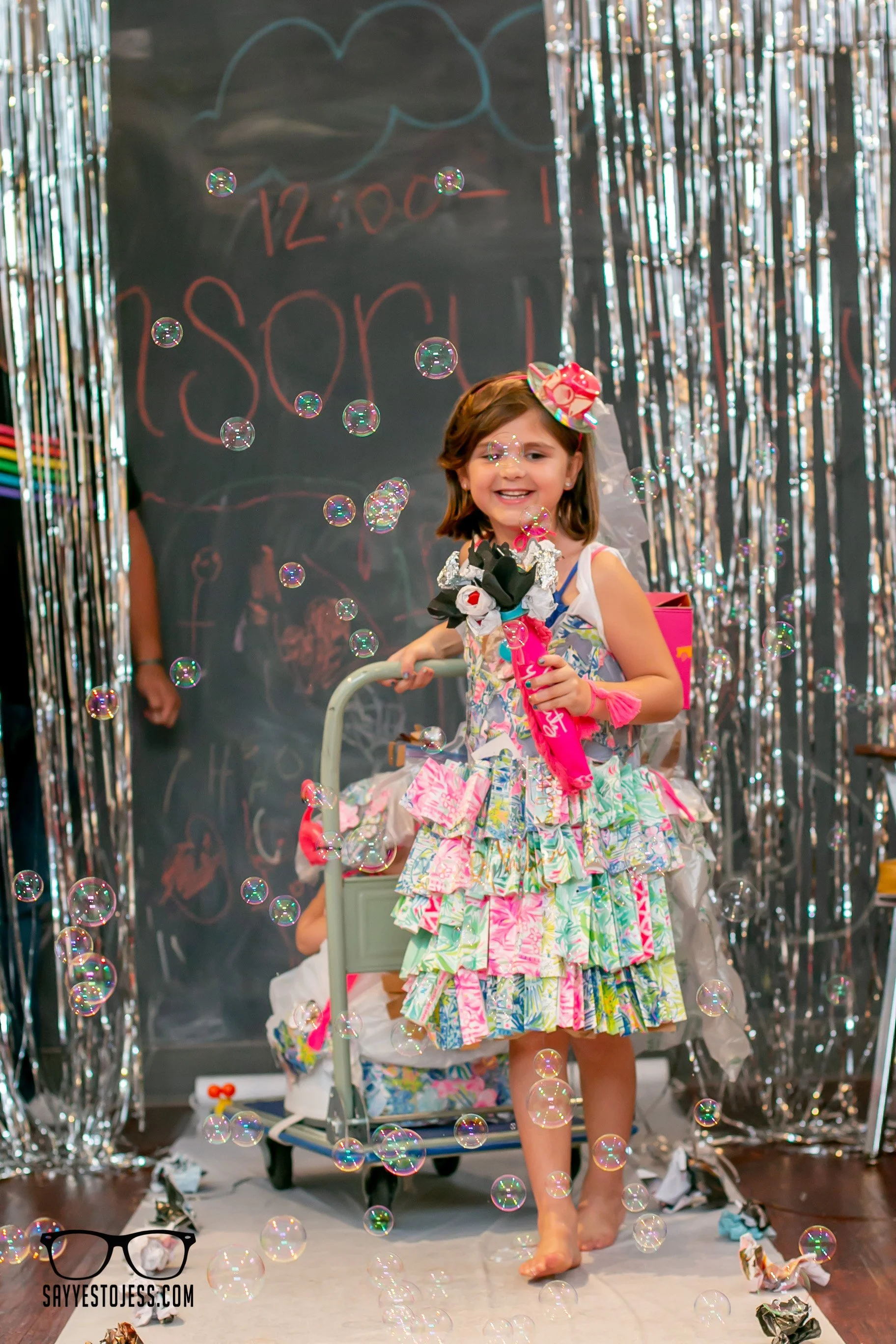 Girl in colorful handmade recycled dress smiling on the runway with bubbles at the kids trashion show at Red Balloon Cafe in Cincinnati