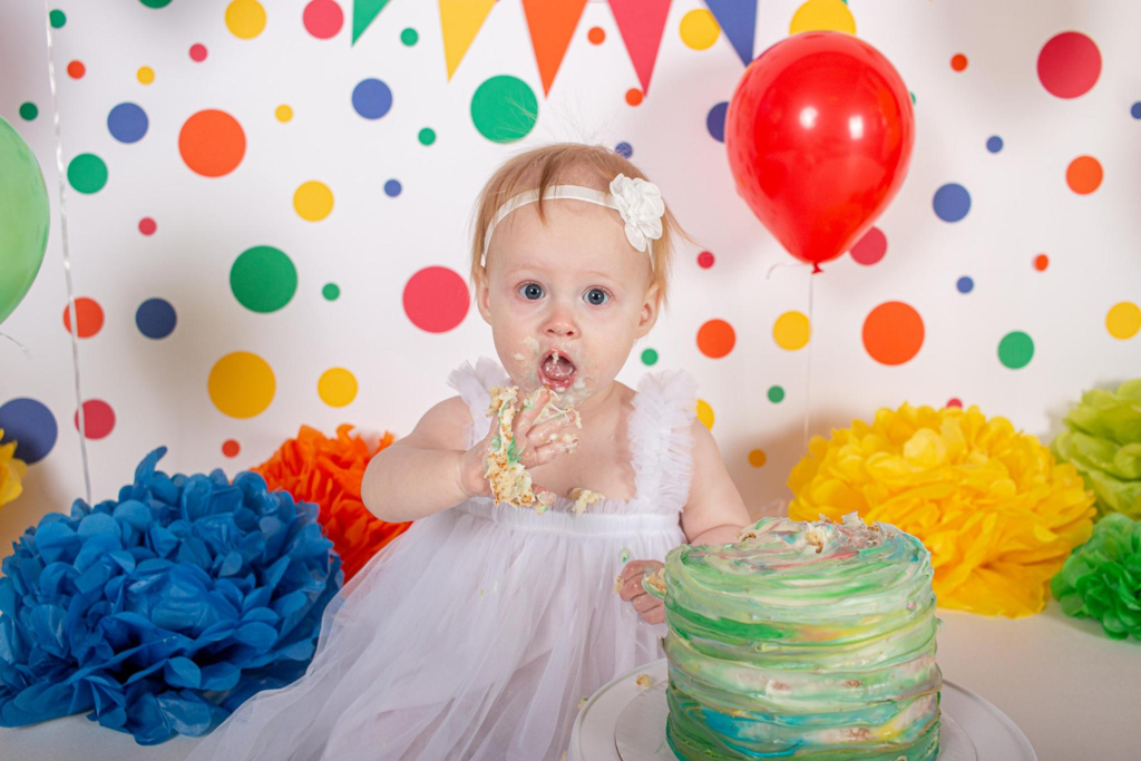 Cincinnati cake smash photographer capturing a baby girl's 1st birthday session with a colorful studio backdrop