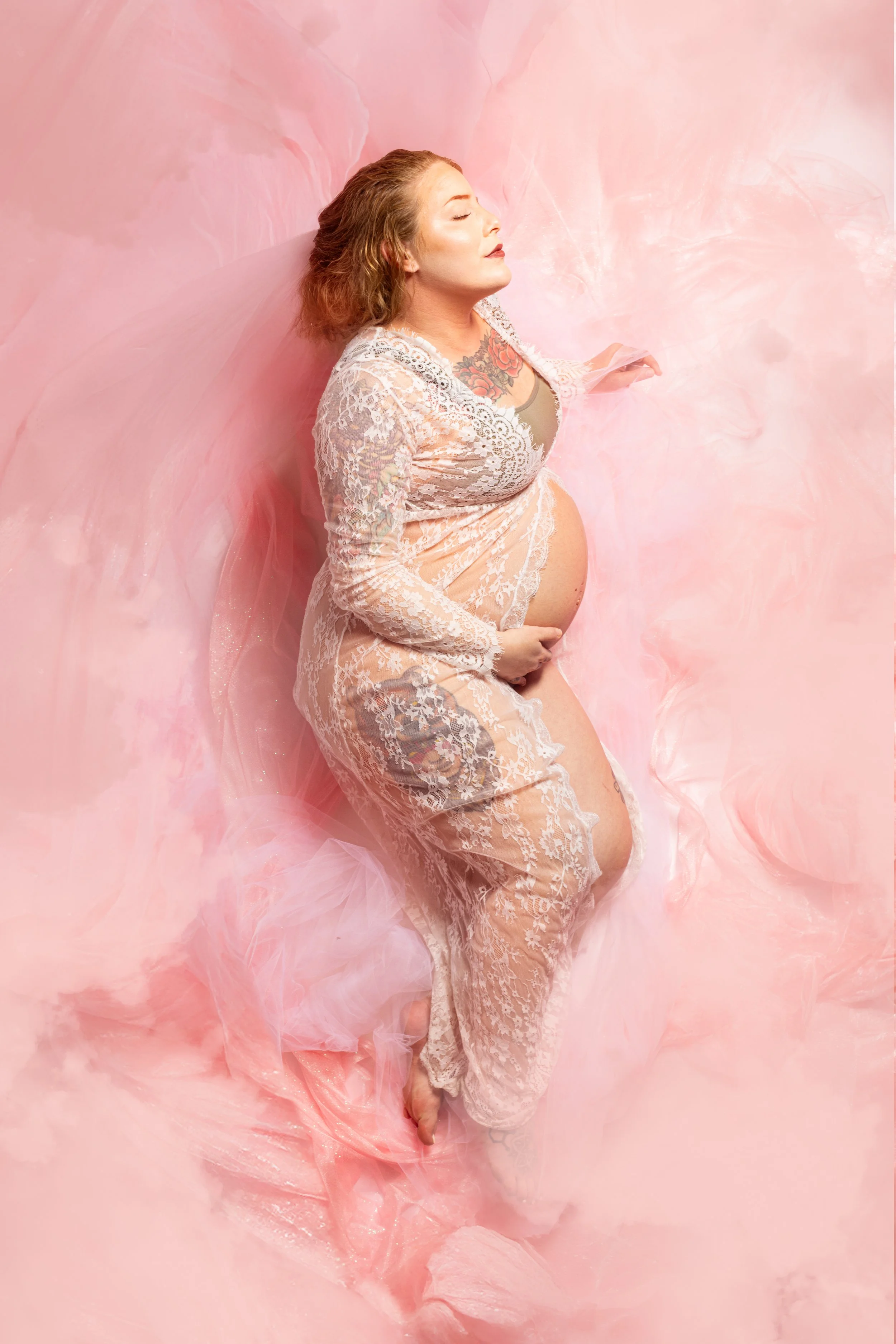 Stunning pink milk bath maternity photoshoot with pregnant woman in white lace gown floating in pink water at Say Yes to Jess Cincinnati photography studio